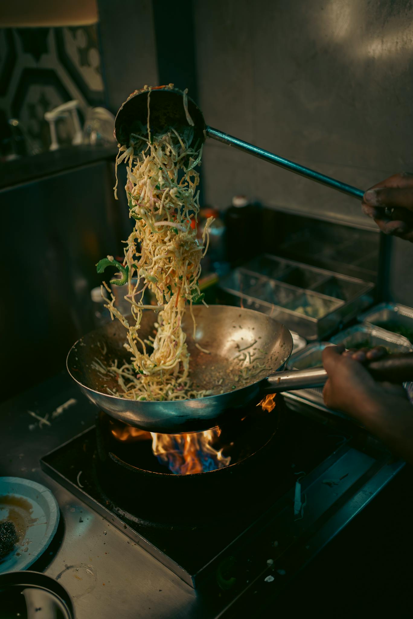 Chef skillfully tosses noodles in a wok over open flames, creating a dynamic culinary scene.